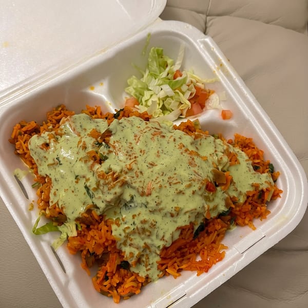 Orange rice with green sauce and a side of lettuce and diced tomatoes in a white takeout container.