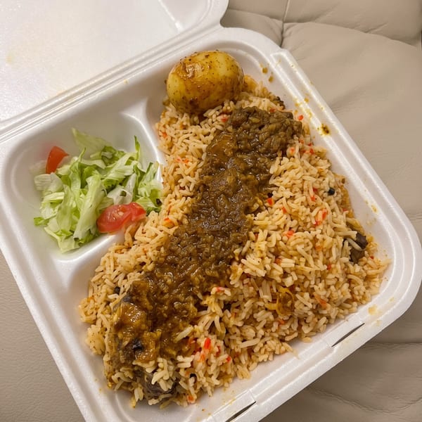 Biryani rice with curry, a boiled egg, and a side salad in a white takeout container.