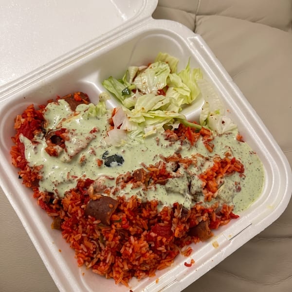 Red rice with meat and green sauce, alongside a small salad, in a white takeout container.