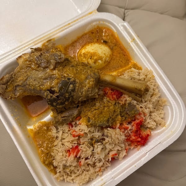 A takeout container holds a lamb shank, rice with red accents, and a hard-boiled egg in curry.